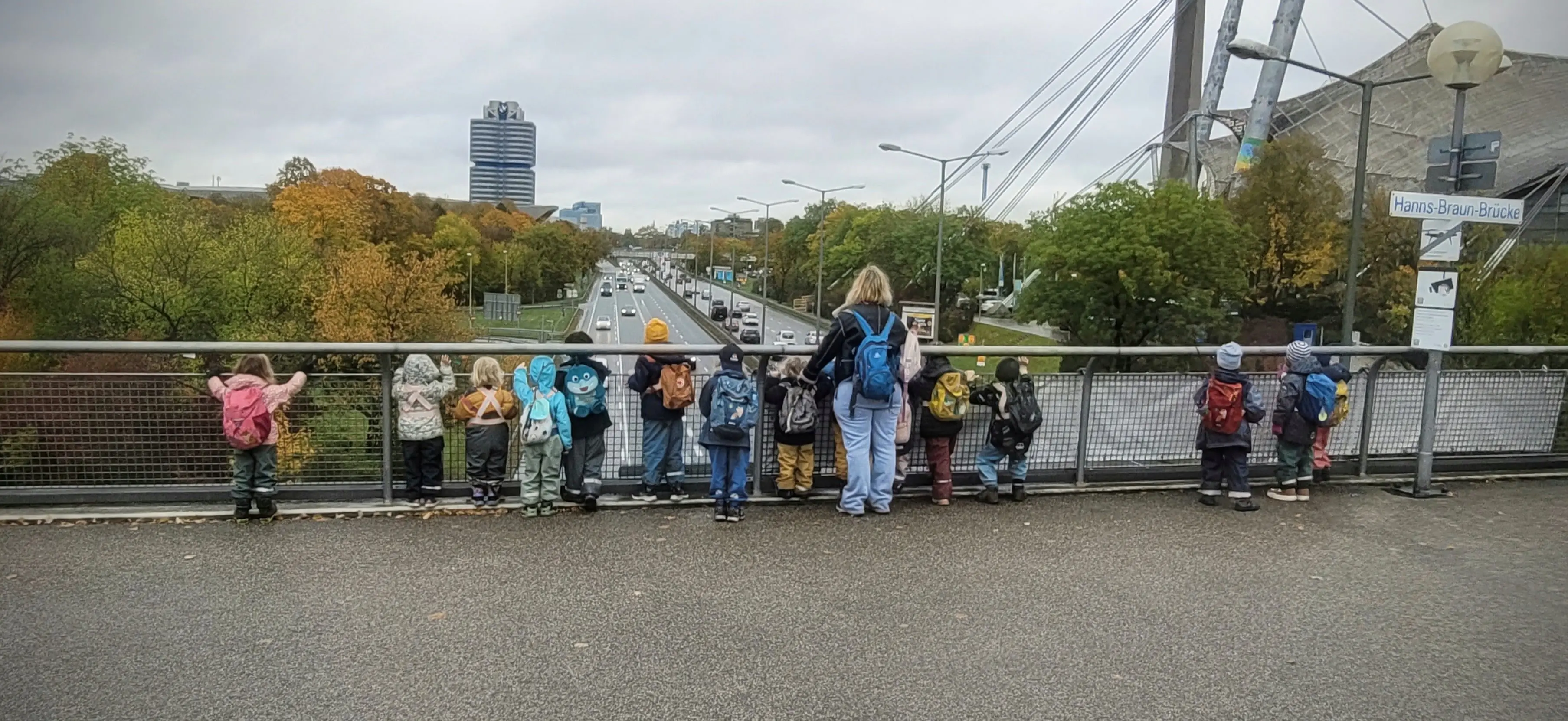 Kinder und Erzieherin der Entdeckerwerkstatt München auf einem Ausflug an der Hanns-Braun-Brücke im Olympiapark
